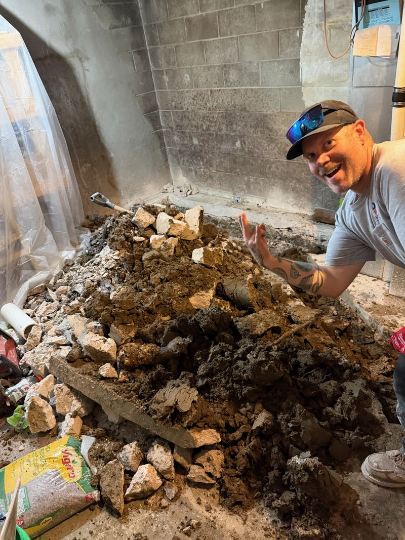 Paragon plumber beside a broken-out basement floor during sewer line repair