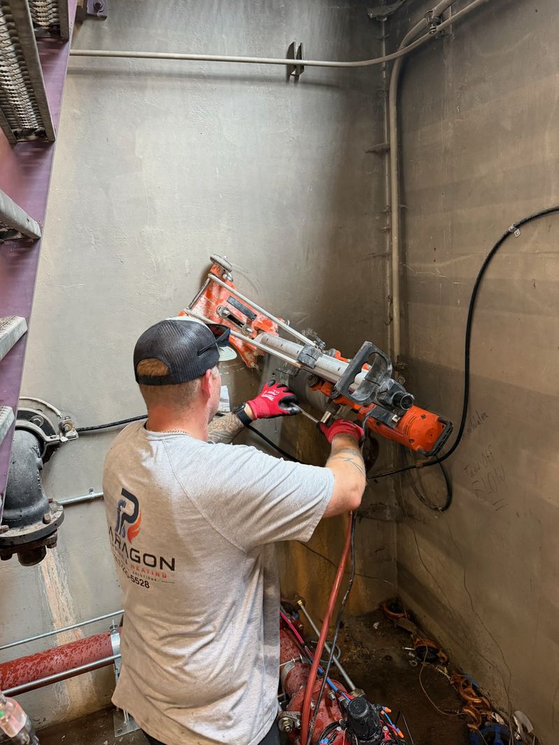 Paragon plumber core drilling a concrete wall in a commercial mechanical room